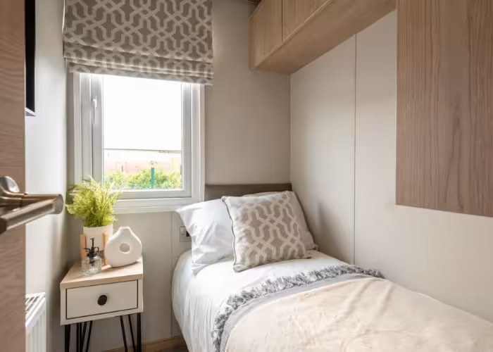 Harraway – Kleine slaapkamer met een eenpersoonsbed, wit beddengoed, kussen en een nachtkastje met planten en decoratie.