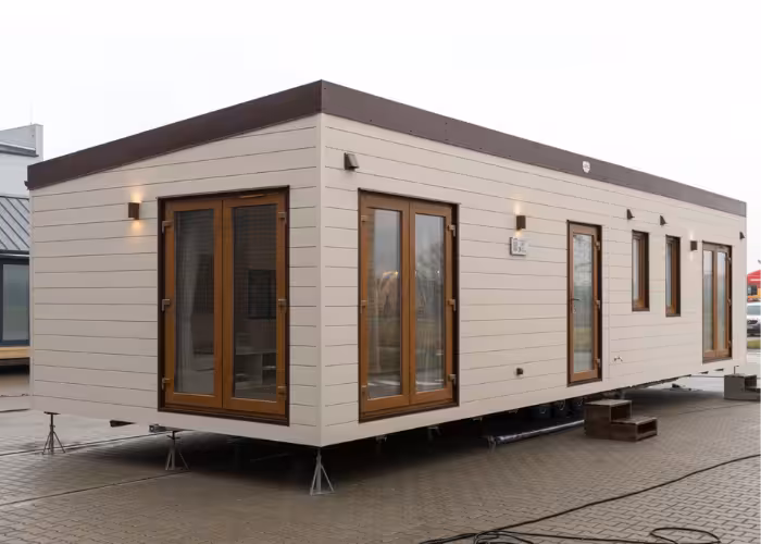 Chios – Modern prefabgebouw met beige gevel en bruin houten ramen, geplaatst op steunen buiten.