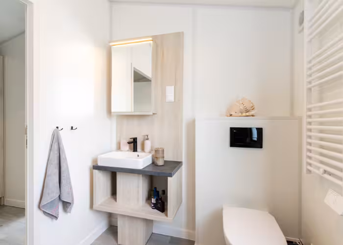 Chios – Lichte, moderne badkamer met een wastafel, spiegelkast, toilet en handdoek op een haak.