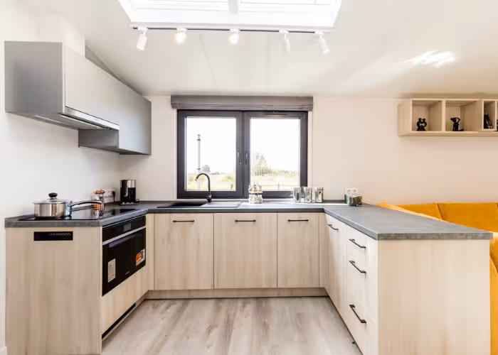 Chios – Moderne lichte keuken met houten kasten, zwart werkblad, oven en raam boven de spoelbak.