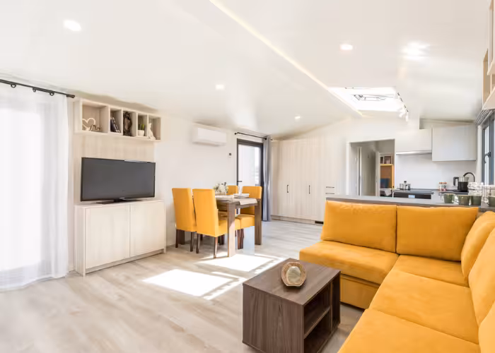 Chios – Lichte woonkamer met oranje hoekbank, eettafel met oranje stoelen en televisiemeubel.