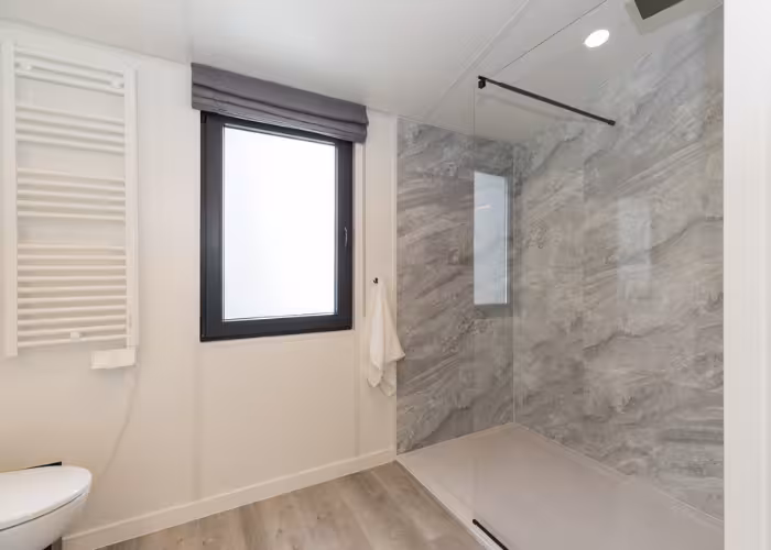Chios – Moderne badkamer met grote glazen inloopdouche, grijze marmeren muren en houten vloer.