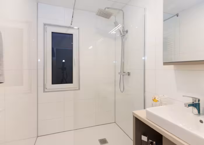 Joli – Moderne badkamer met een glazen douchecabine, regendouche, wastafel en spiegelkast.