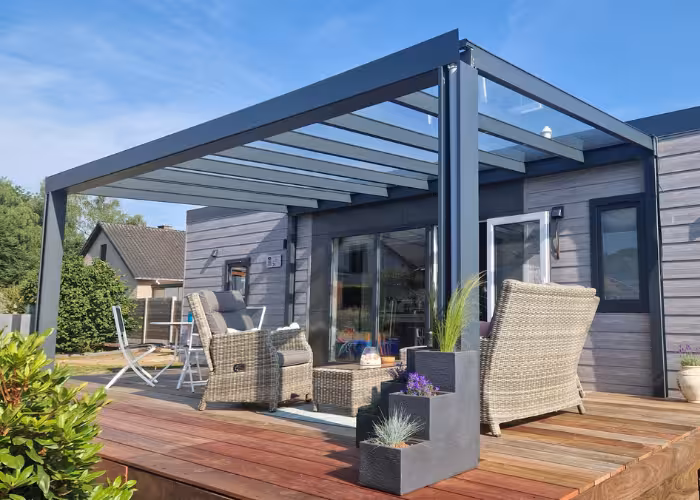 Joli – Modern houten terras met grijze pergola, rotan stoelen, planten en open schuifdeur.