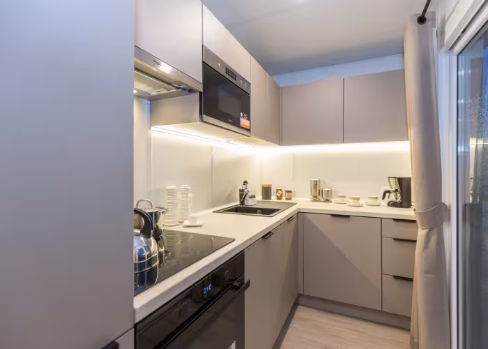Joli – Moderne keuken met hoekspoelbak, inductiekookplaat, magnetron en koffiezetapparaat naast glazen deur.