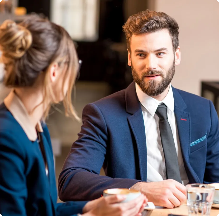 Two business professionals having a conversation over coffee at a table.