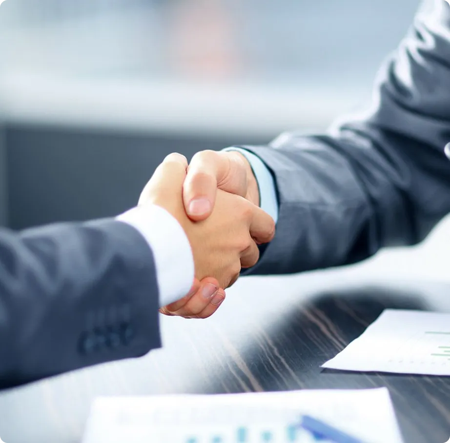 Two business people shaking hands over a table with documents.
