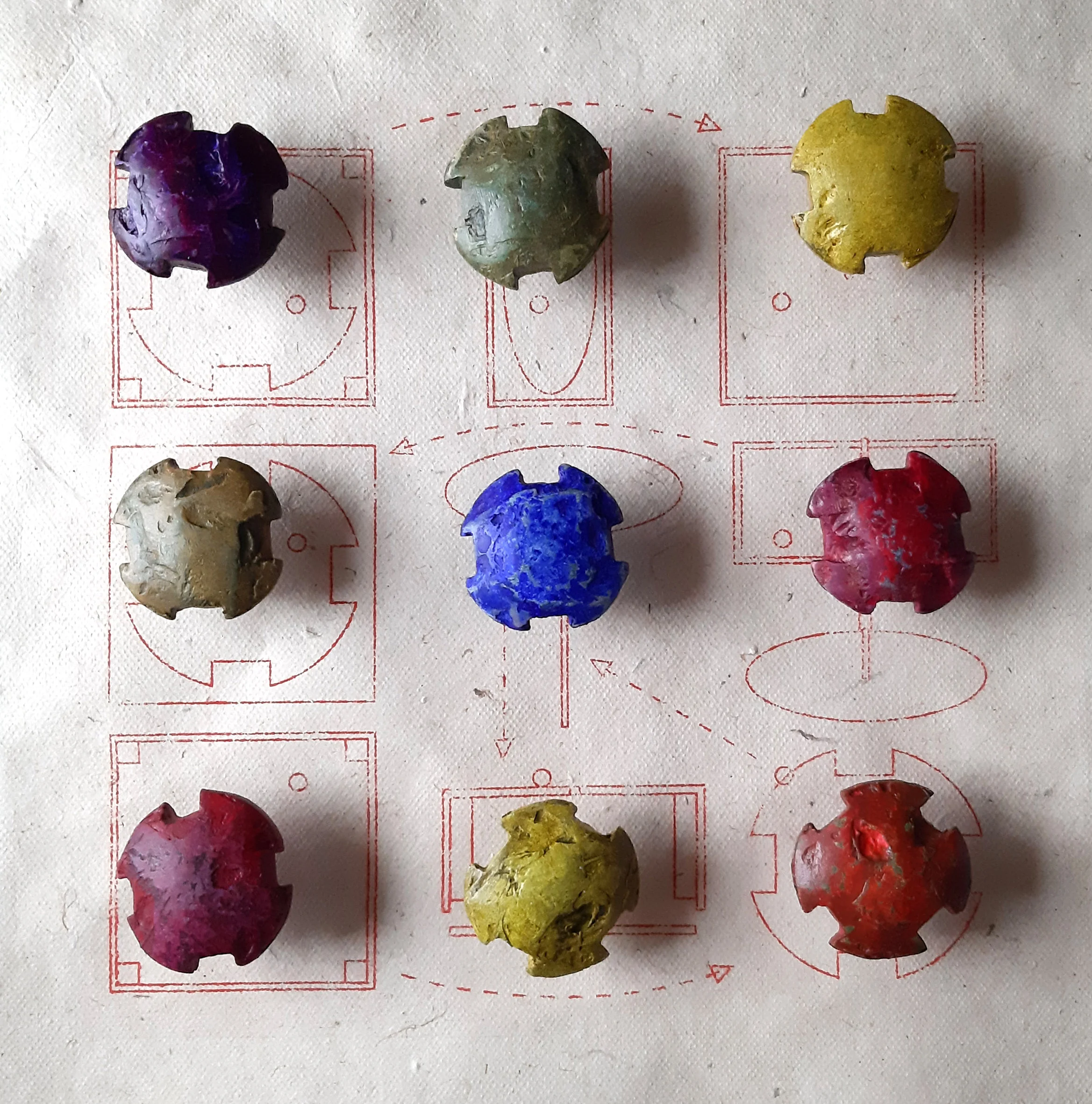 Färgglada fossila stenar arrangerade i ett 3x3 rutnät på ett tyg med röda diagram och pilar.