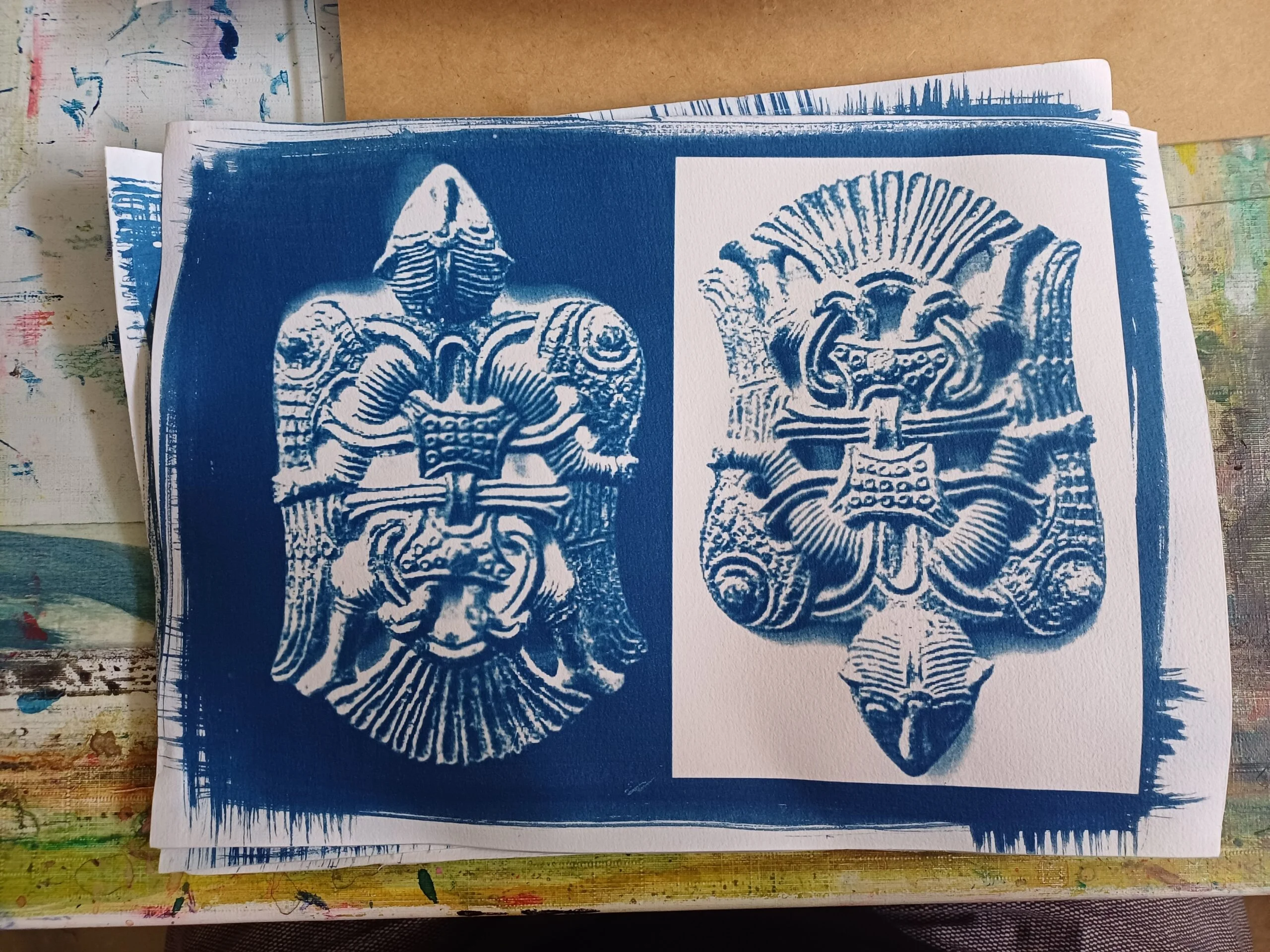 Två blå-vita tryck av detaljerade, symmetriska prydnadsmotiv med fågel- och växtinspirerade former på papper.