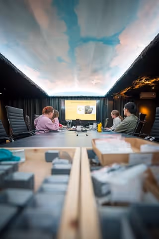 Fyra personer i ett mötesrum som tittar på en presentationsskärm vid ett bord.