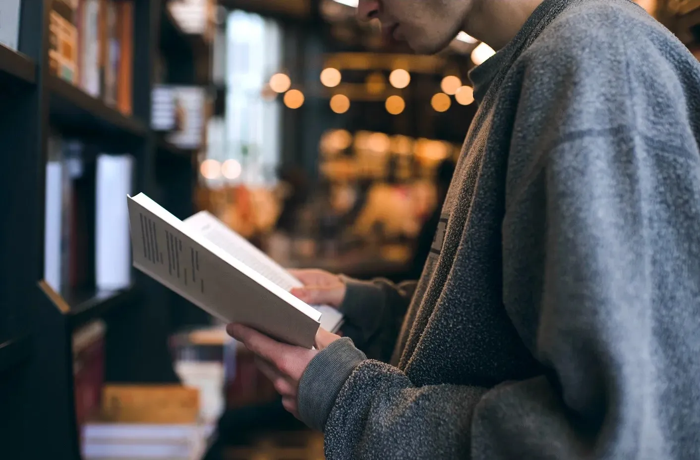 adolescent standing with a book reading it at a book store.