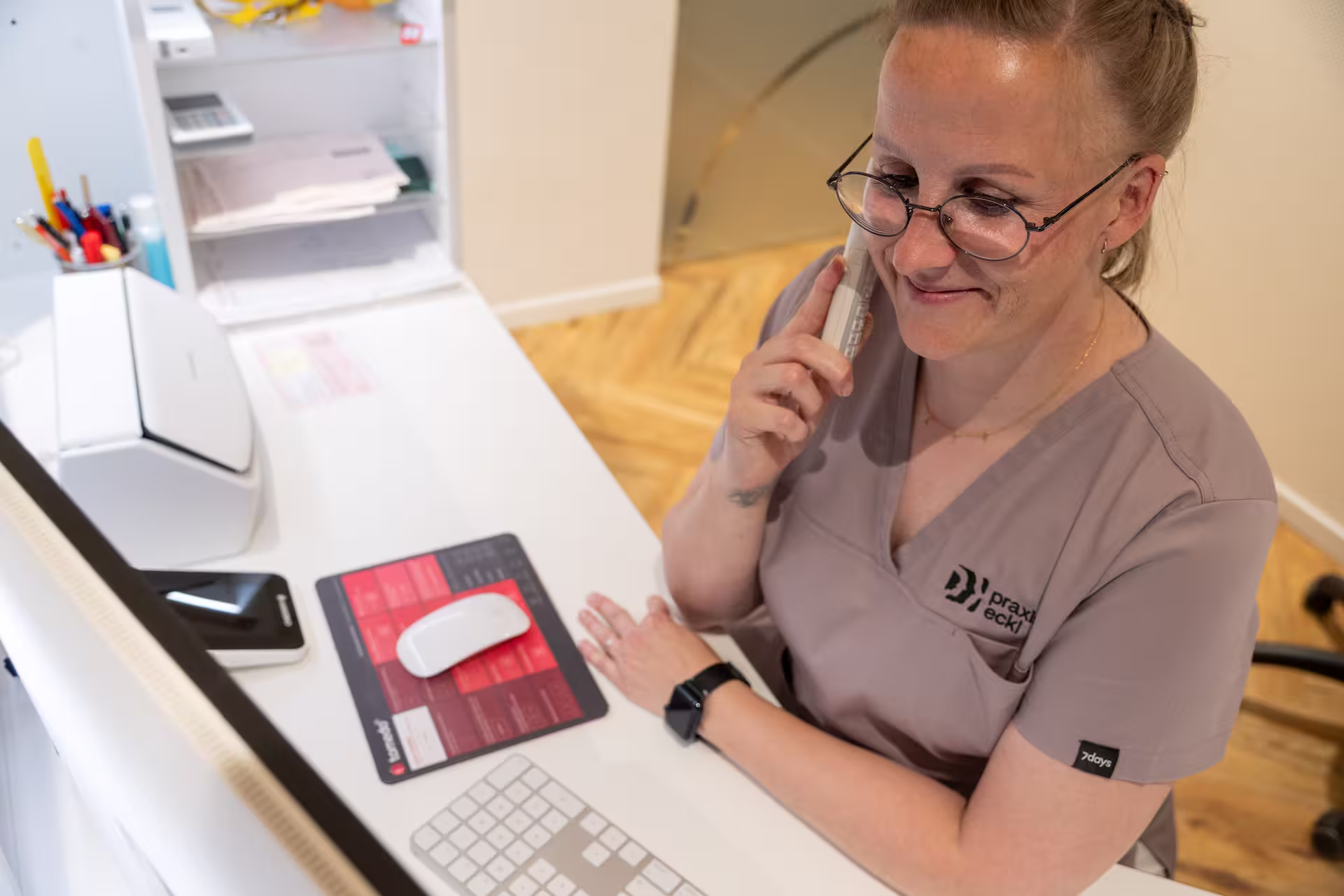 Eine medizinische Fachangestellte telefoniert mit den Patienten am Empfangtresen.