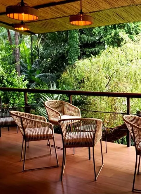 Outdoor wooden deck with wicker chairs and hanging lights overlooking lush green tropical plants.