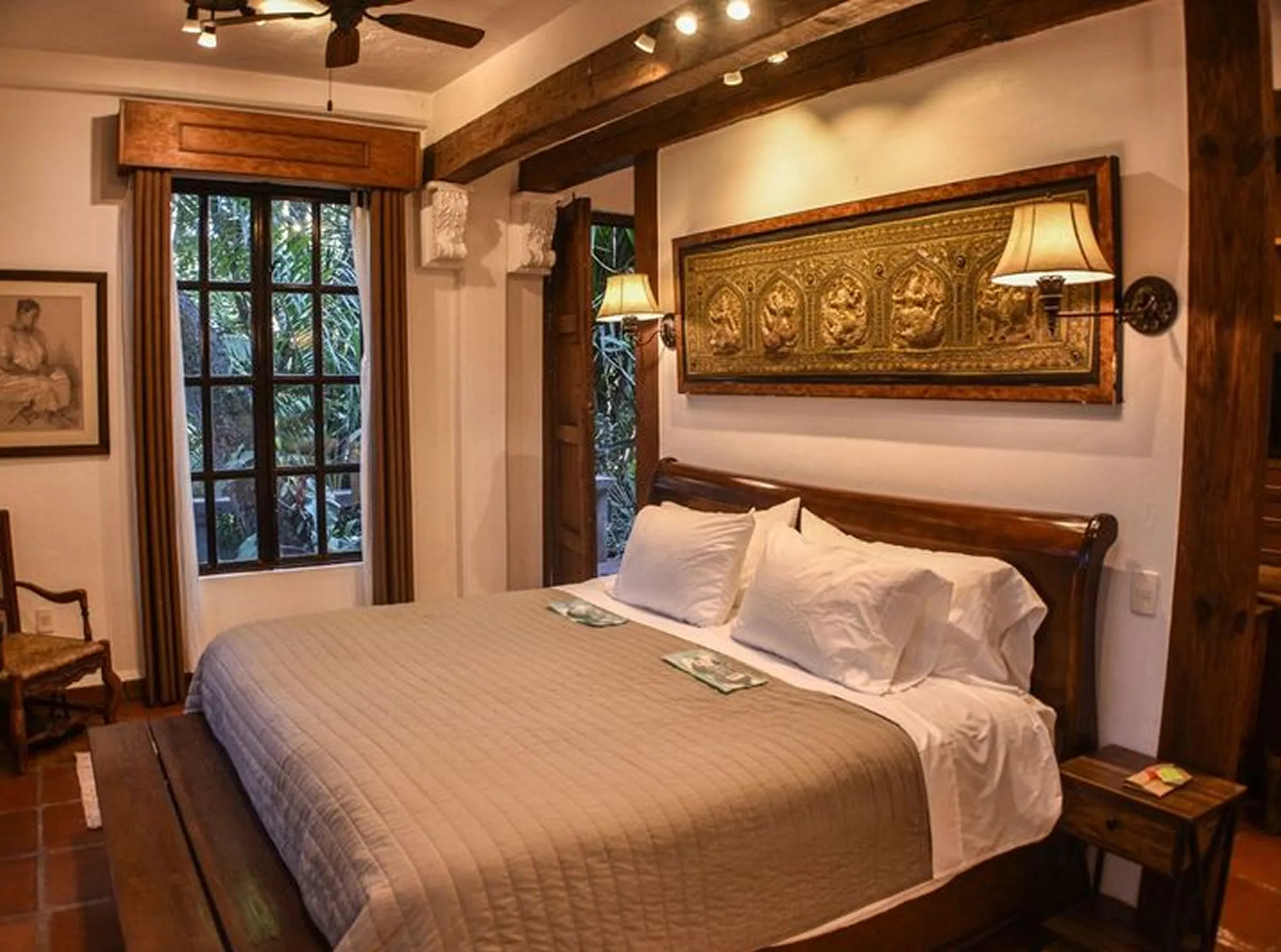Cozy bedroom with a large wooden bed, beige quilt, white pillows, wall-mounted lamps, and a decorative gold panel above the headboard.