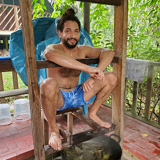 Man sitting relaxed in a wooden steam sauna chair with steam rising from a pot below.