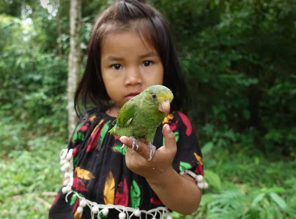 Young girl holding a green parrot with a blurred forest background.