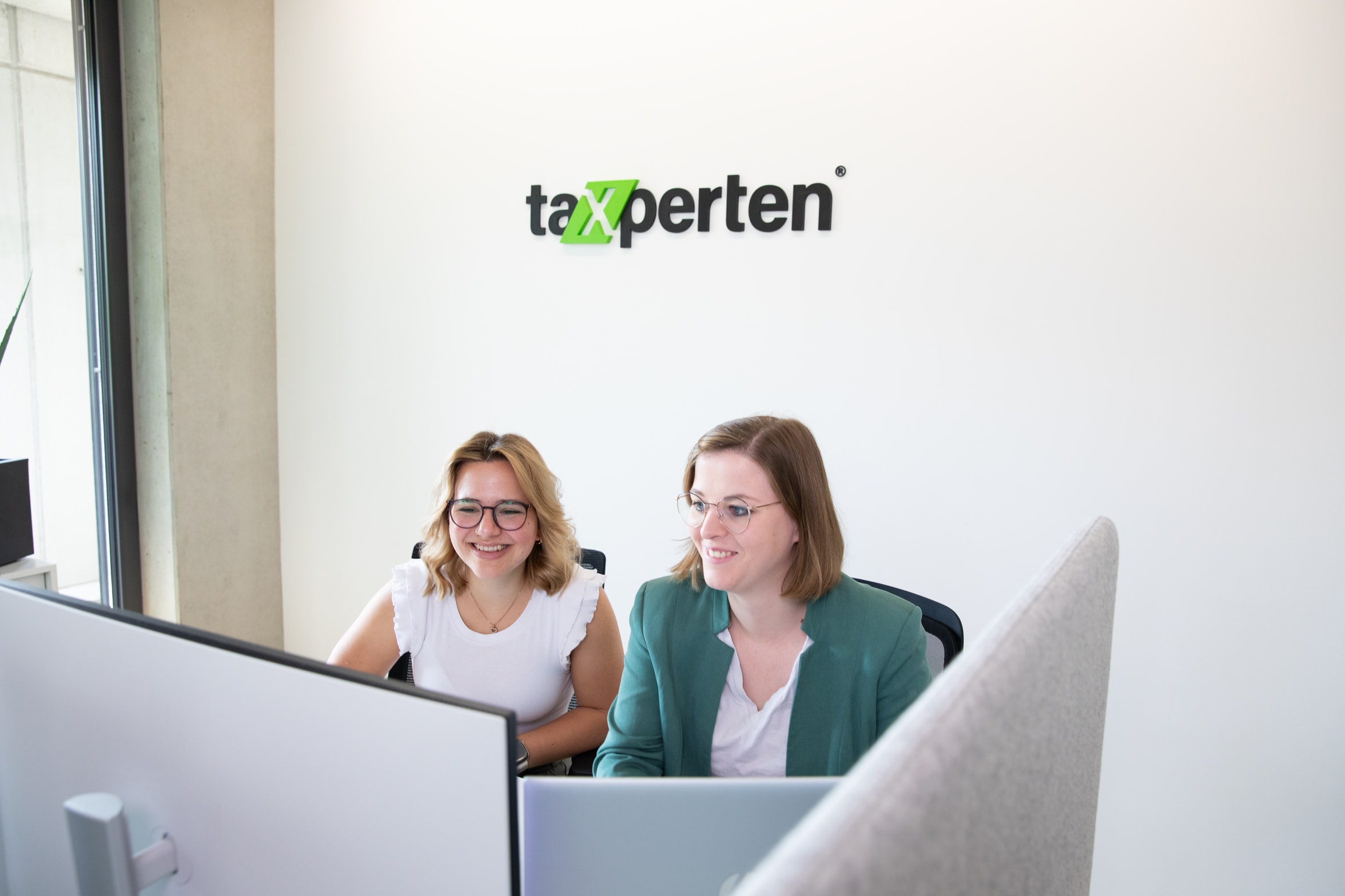 Team stimmt Lohnbuchhaltung ab – zwei Kolleginnen besprechen Payroll-Prozesse digital.