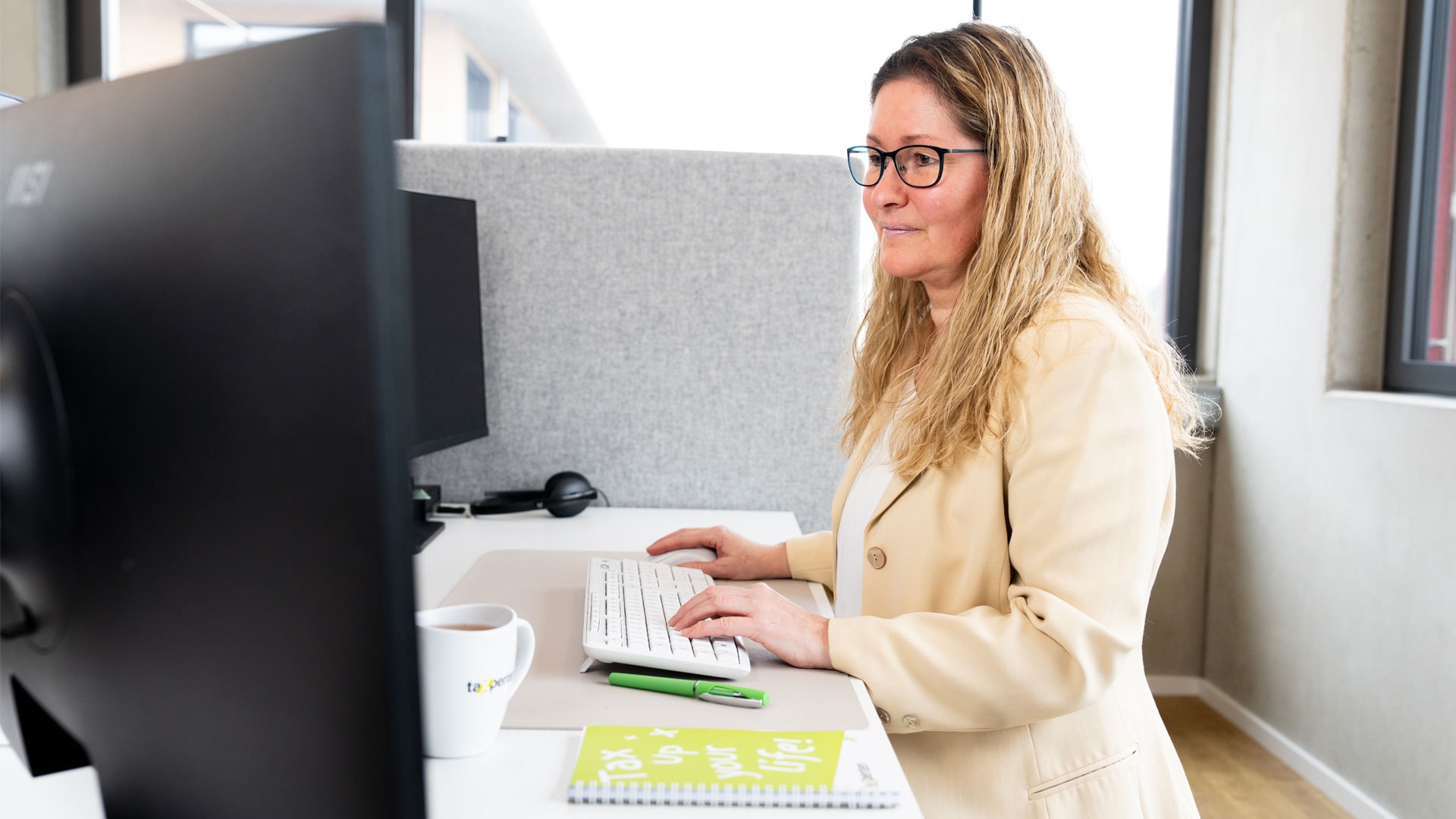 Mitarbeiterin arbeitet konzentriert am Schreibtisch mit Computer und Notizbuch.