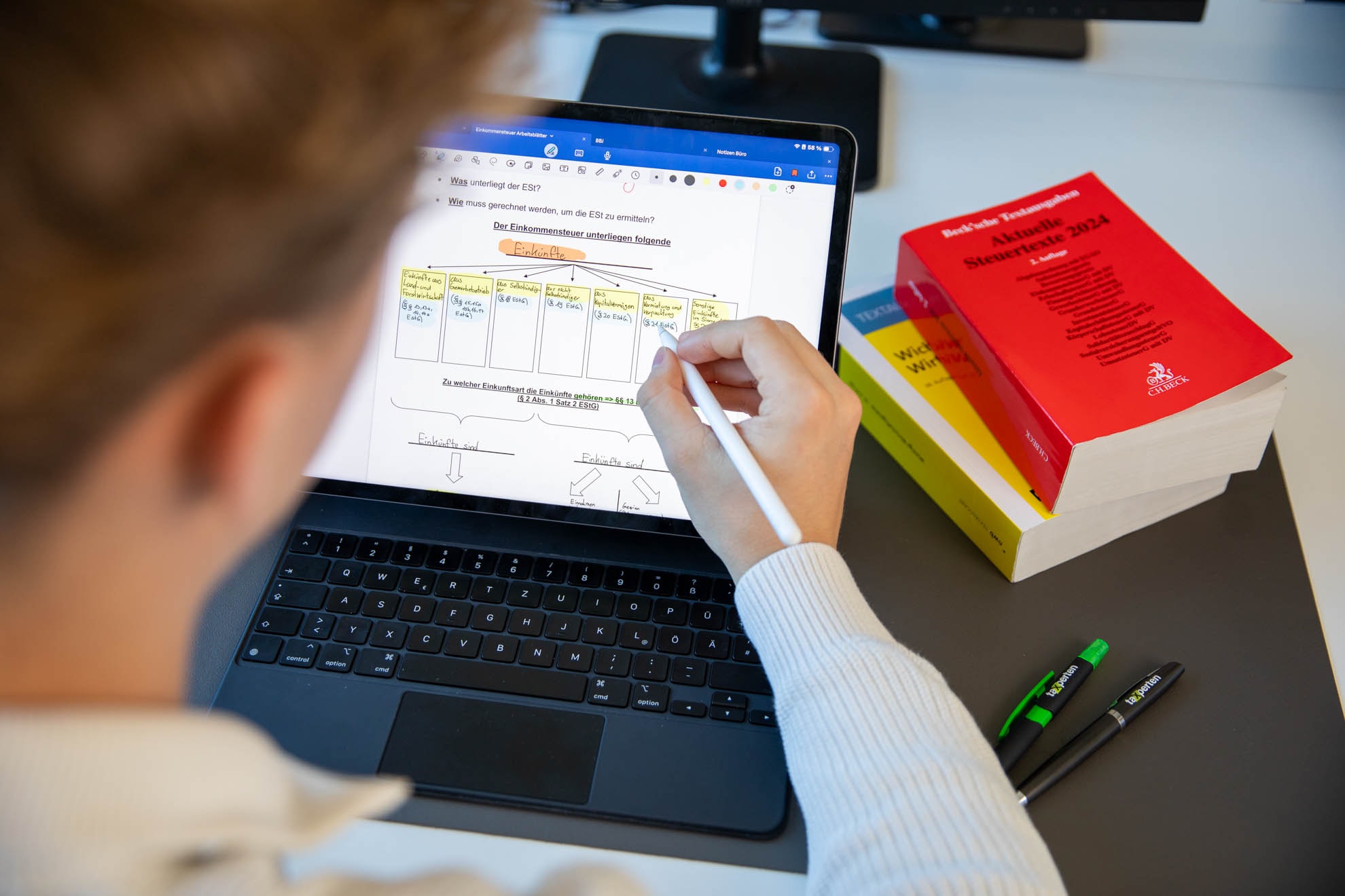Student lernt für das Steuerstudium mit digitaler Einkommensteuer-Grafik und Fachbüchern wie „Aktuelle Steuergesetze 2024“.