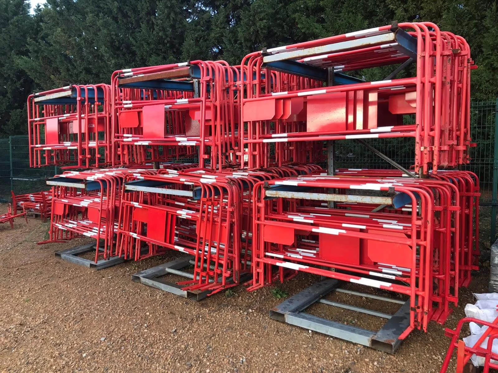 Rack de stockage rempli de barrières de chantier rouges empilées, installé en extérieur sur sol gravillonné.