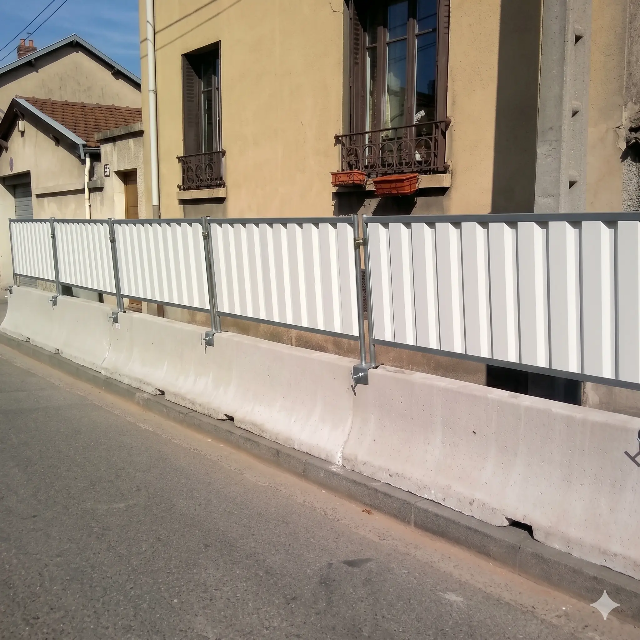 Clôture bardée blanche installée sur blocs béton GBA pour sécurisation de chantier en milieu urbain.