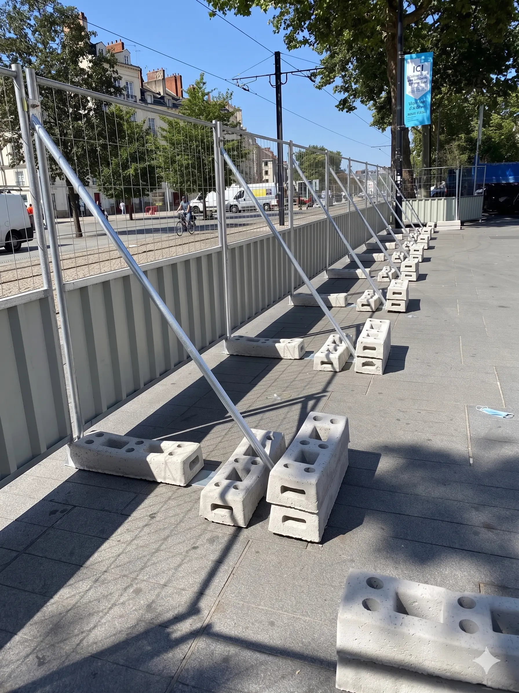 Clôture de chantier avec jambes de force et plots béton assurant la stabilité des barrières sur trottoir en milieu urbain