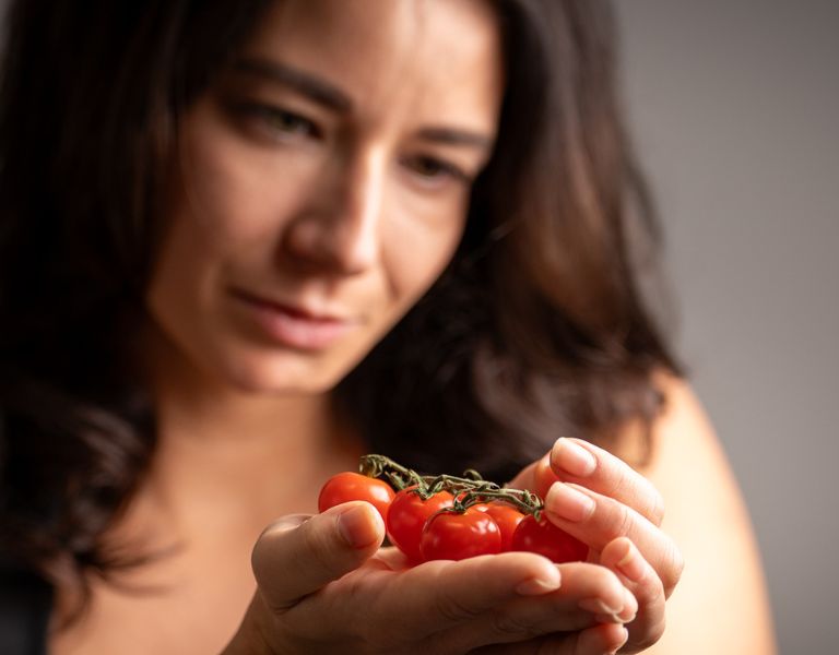 Frau betrachtet nachdenklich eine Handvoll frischer Cocktailtomaten.