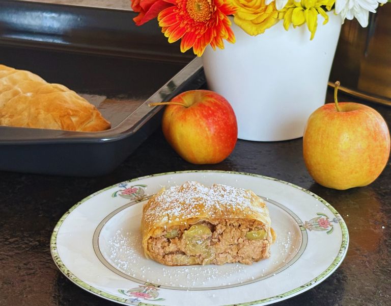 Frischer Weintraubenstrudel, serviert mit Puderzucker und dekoriert mit Äpfeln und Blumen.