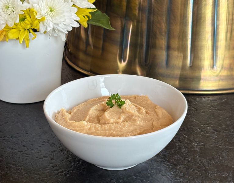 Cremiger Hummus aus Kichererbsen in einer weißen Schale, garniert mit frischer Petersilie.