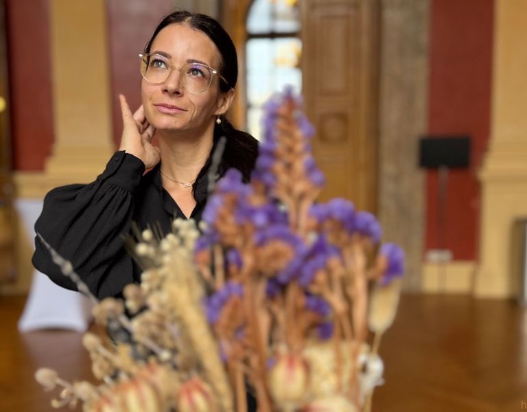 Sarah Hein von Schlicht Vegan blickt nachdenklich zur Seite, im Vordergrund Trockenblumen, elegante Kulisse in Wien – Veganuary 2026.