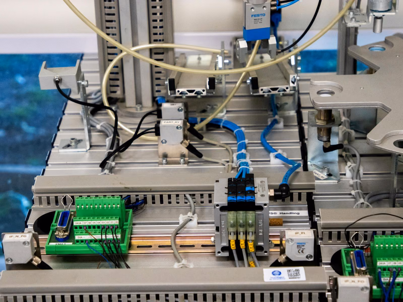 Close-up of an industrial automation setup featuring electrical components, wiring, blue pneumatic tubes, and a FESTO-labeled device mounted on a metal frame.