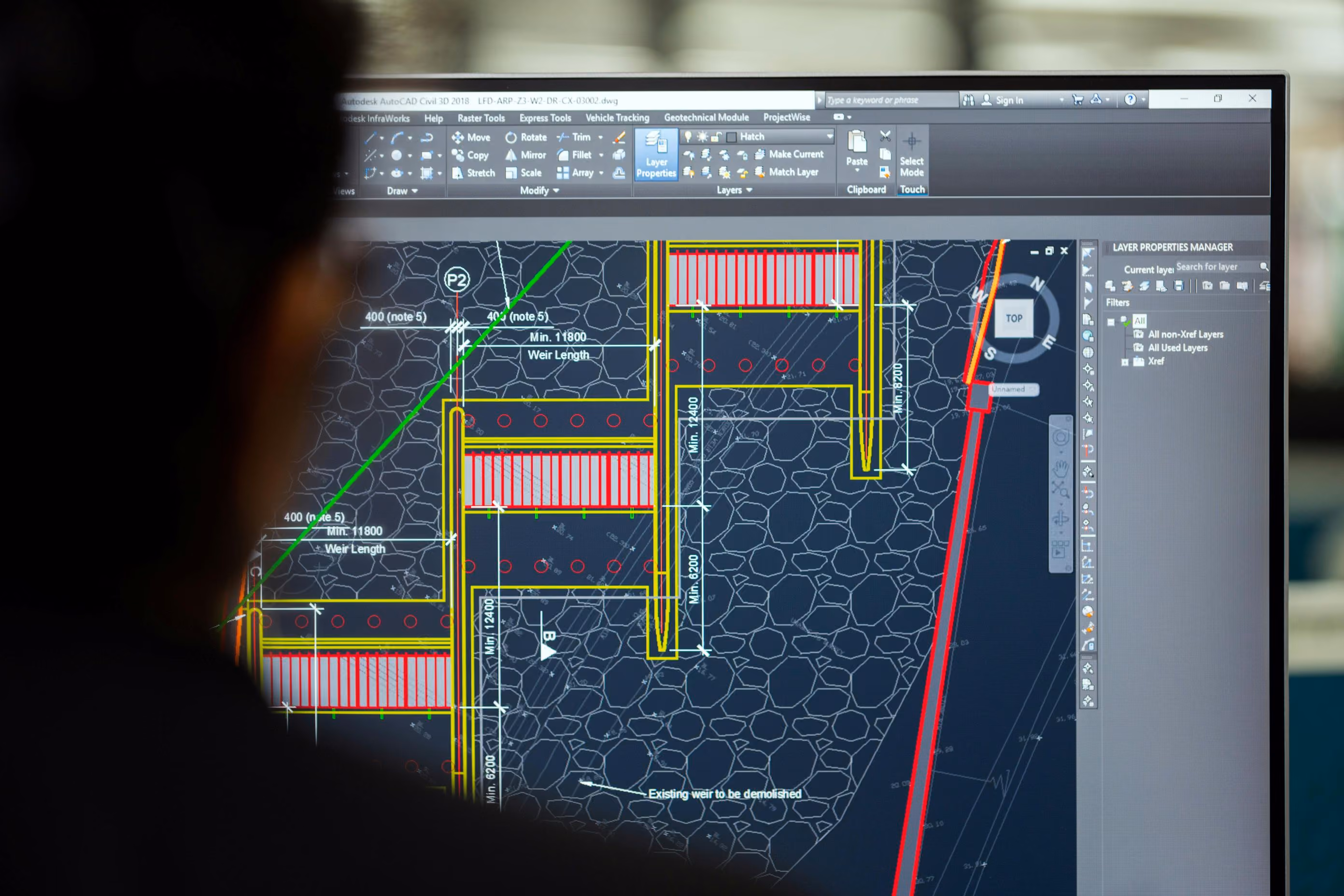 Computer screen displaying an AutoCAD civil engineering drawing with measurements and layer properties, viewed over the shoulder of a person.