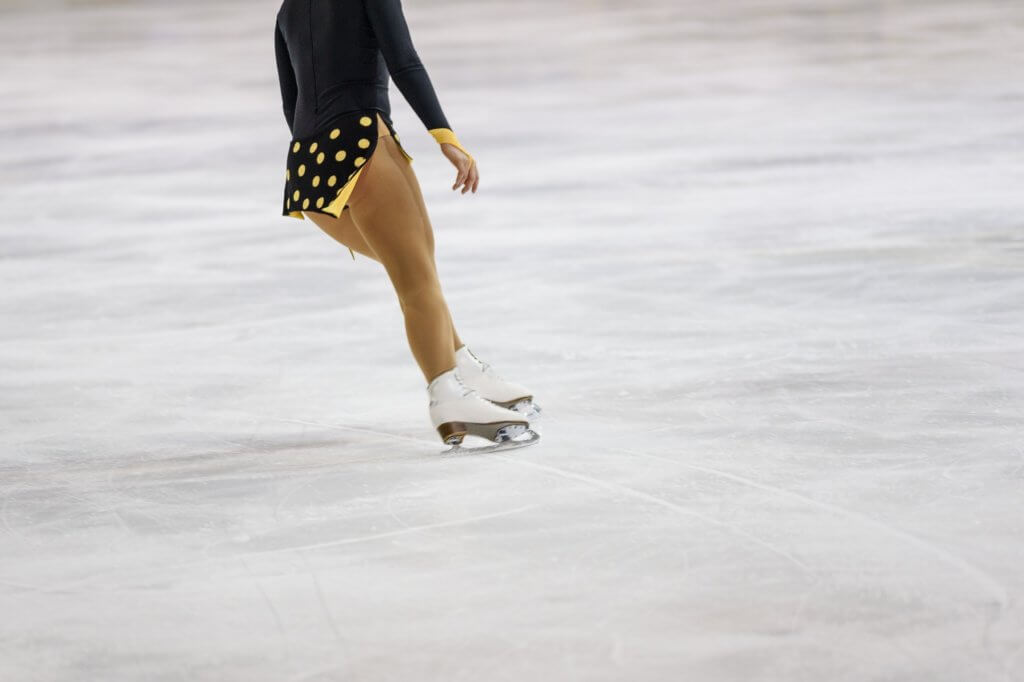 Female figure skater glides alone on the ice, wearing white figure skates.