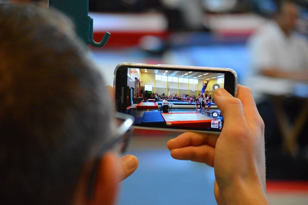 Father filming his daughter doing gymnastics.