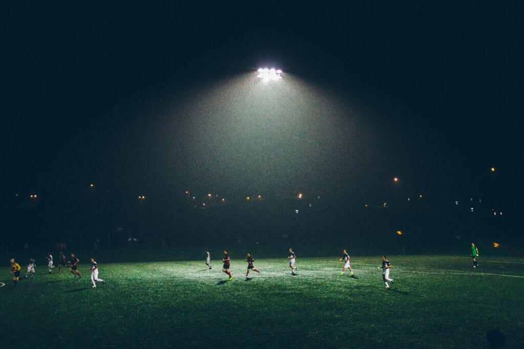 Soccer players playing on a soccer field at night.