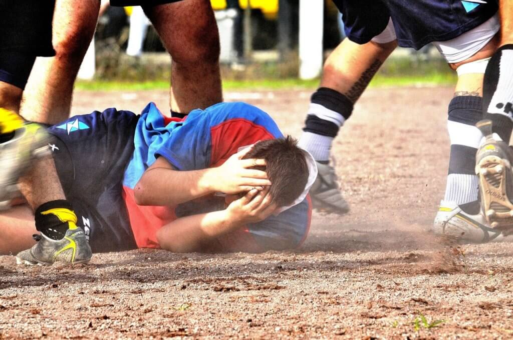 Rugby athlete grabbing his head illustrating concussion risks.