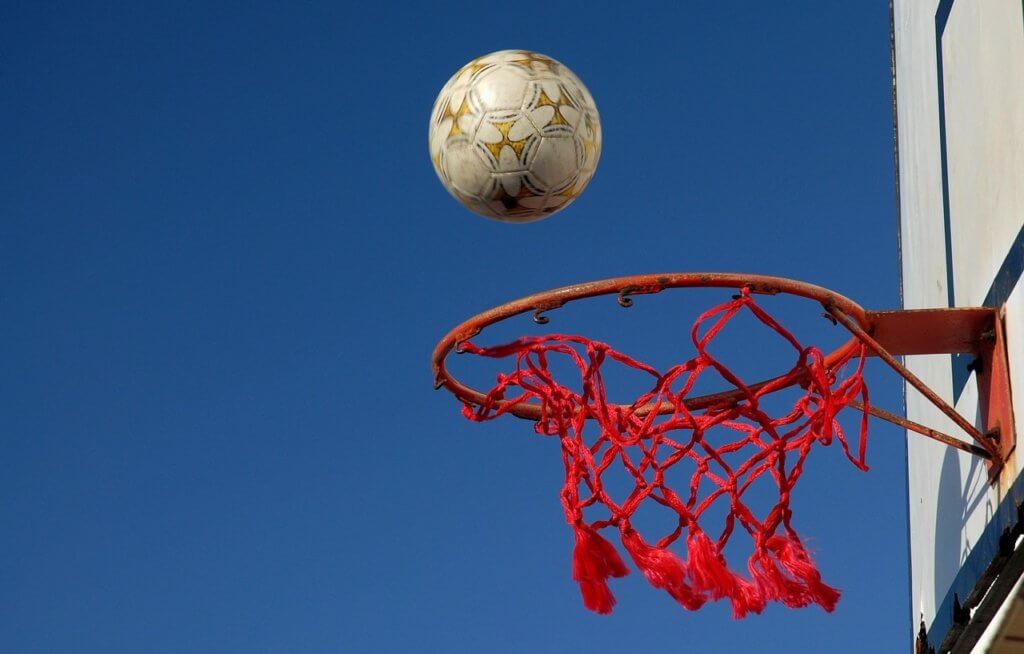 Playing multiple sports at once. A Soccer ball bounces off a basketball rim