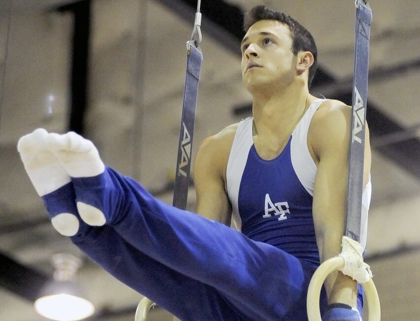 Man performs pike on rings showing that core strength is one of the benefits of gymnastics