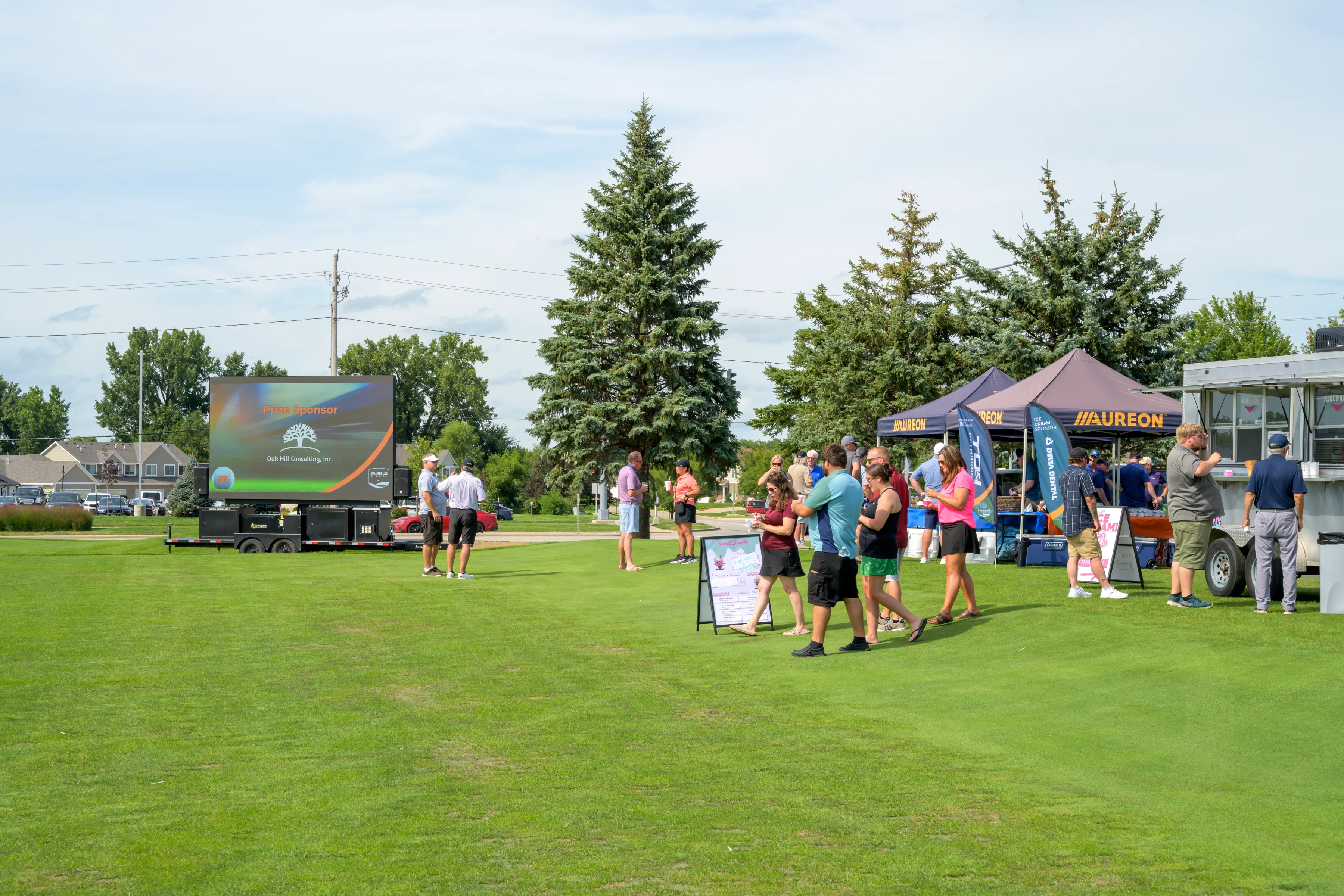 People stand near a large outdoor LED screen showing a sponsorship logo.
