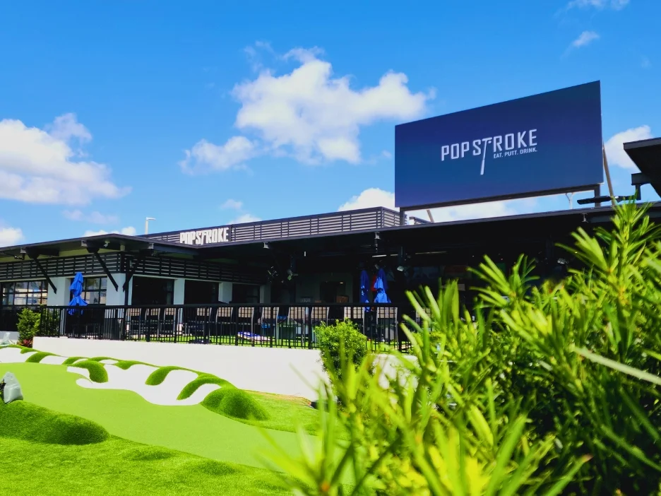 A modern building with a large sign for PopStroke, featuring mini golf and outdoor seating. 