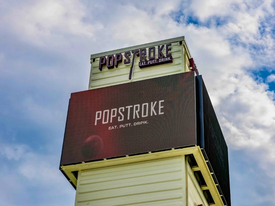 A tall sign for PopStroke, showing the logo and the text 'EAT. PUTT. DRINK.' against a cloudy sky. 