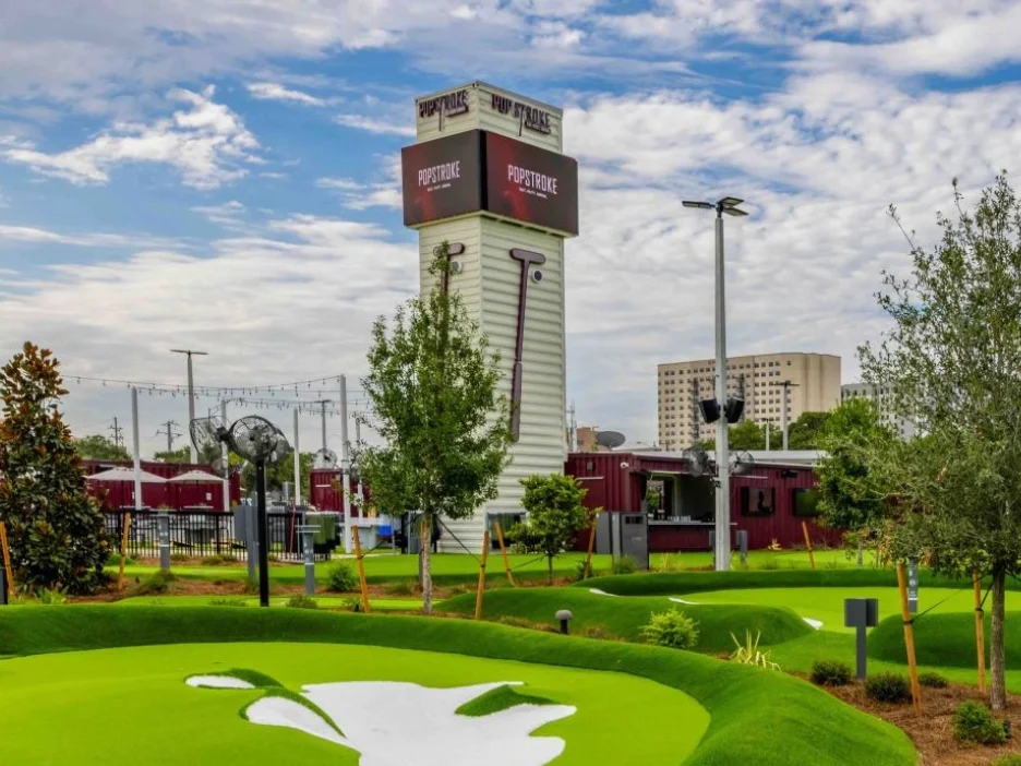 A colorful mini-golf course with bright green turf, trees, and a tall sign reading 'PopStroke'. 