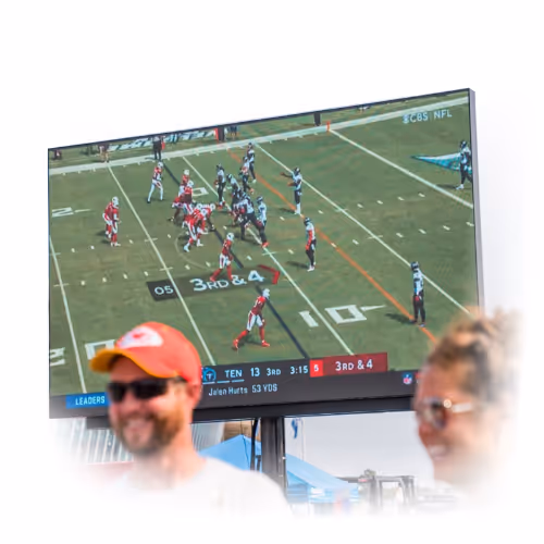 Outdoor large screen showing an American football game with players in red and black uniforms lining up at the 10-yard line.