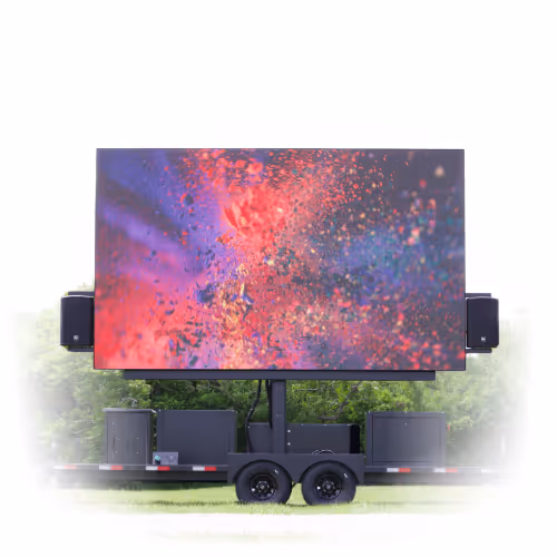 Large outdoor LED screen displaying colorful red, purple, and blue abstract visuals mounted on a trailer with speakers on either side, set on grass with trees in the background.