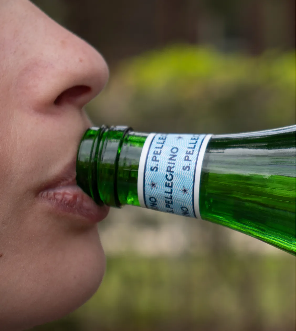 Close up of person drinking from san Pellegrino bottle
