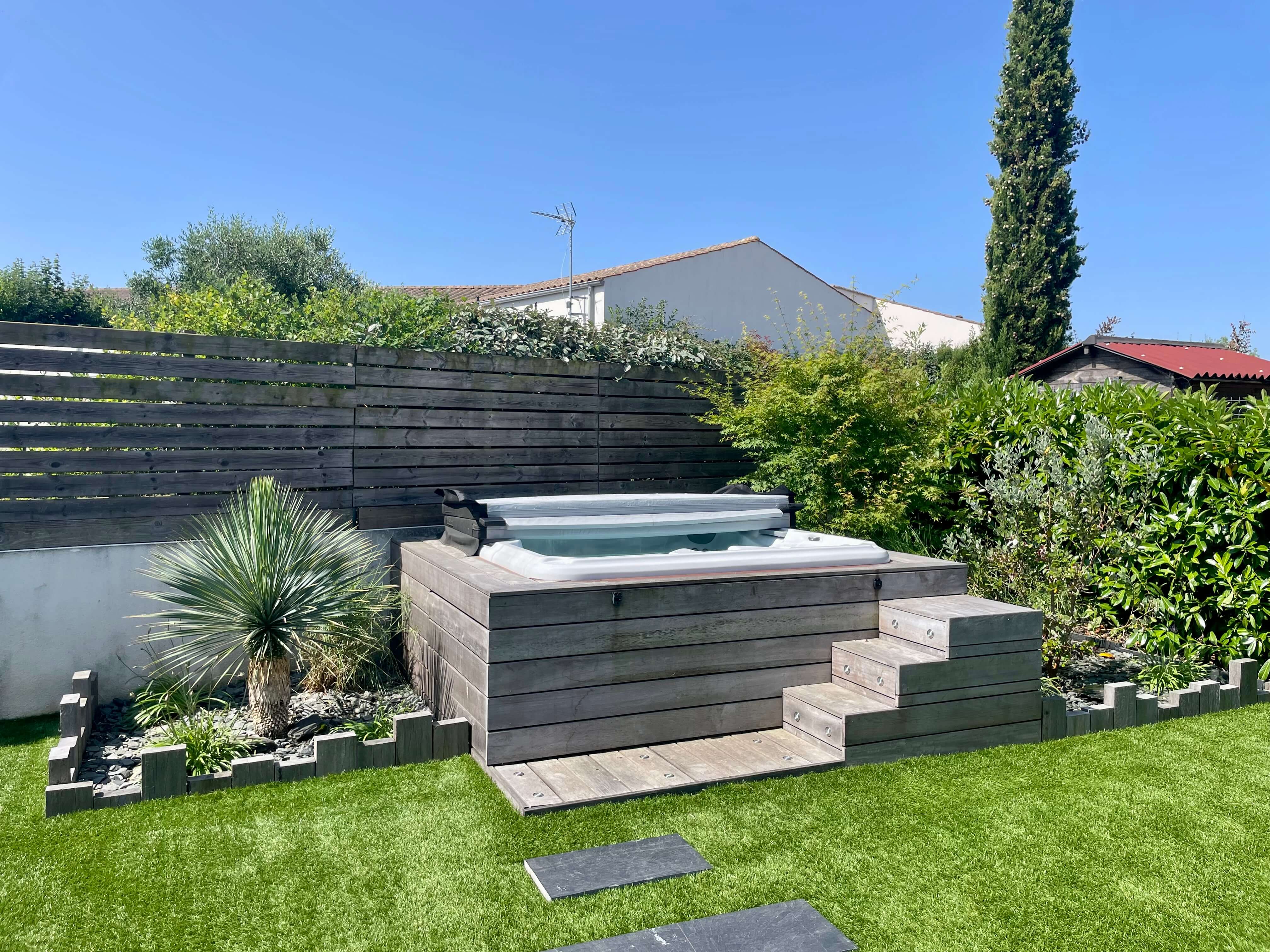 Installation d’un spa encastré dans une terrasse en bois exotique avec jardin paysager et gazon synthétique