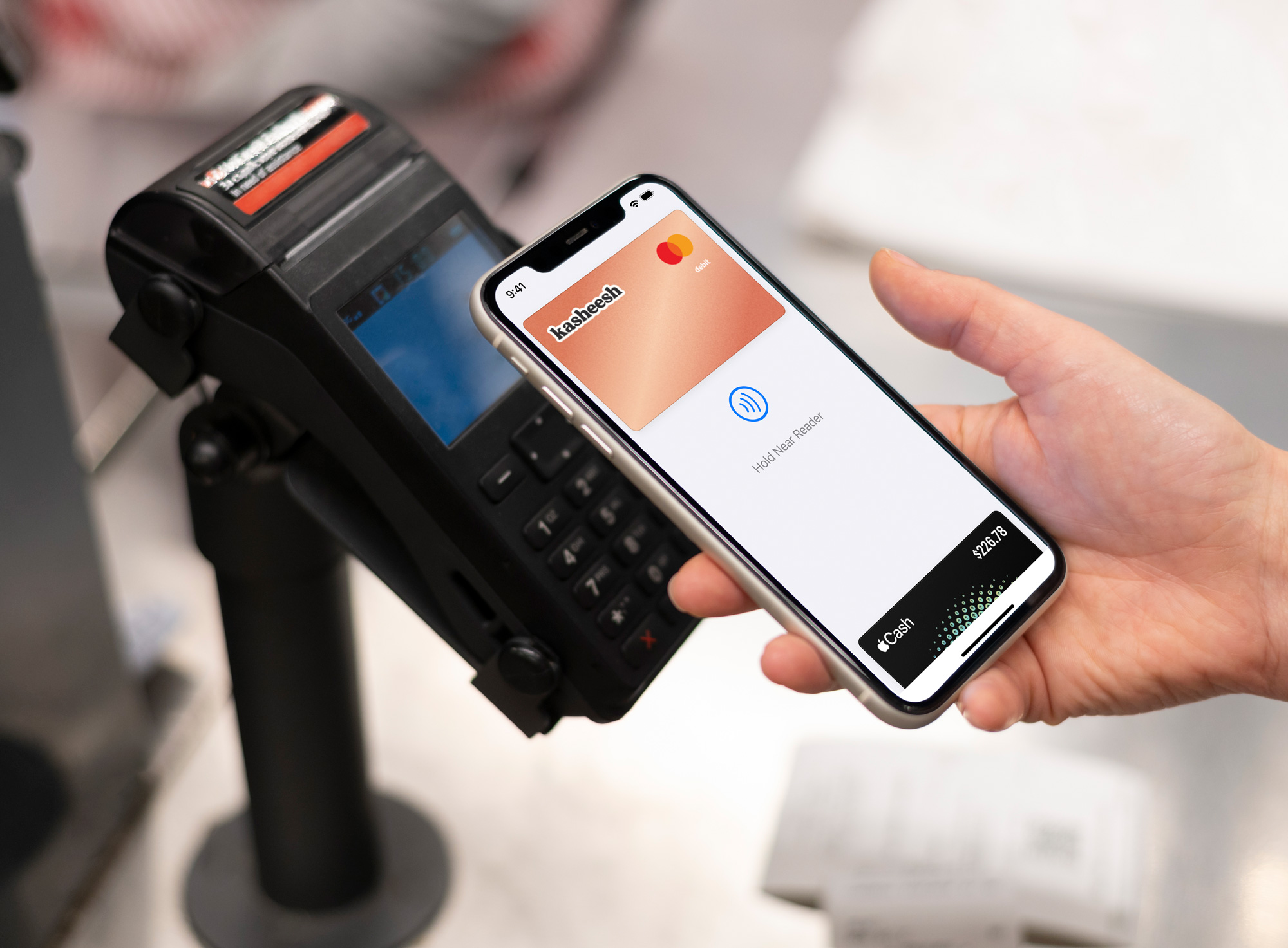 The digital Kasheesh Card being used to pay with Apple Pay on an iPhone beind held by a hand over a payment terminal with tap-to-pay
