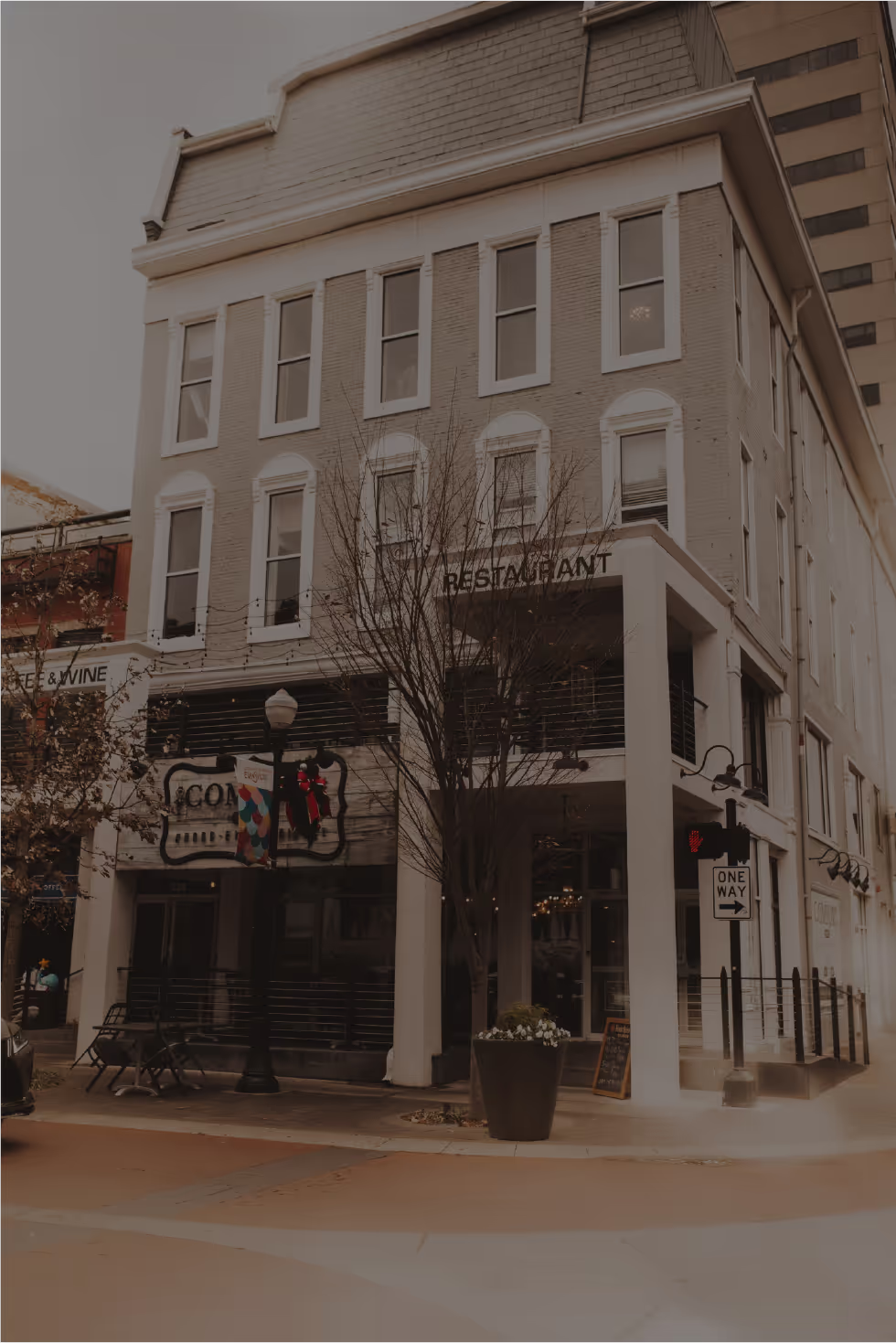 Comfort- a stylish brick restaurant with a festive wreath, surrounded by trees and outdoor seating, in an urban setting.