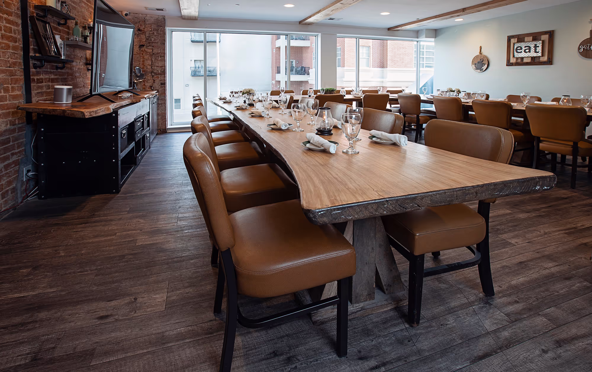 A modern dining room with a long wooden table, leather chairs, and large windows, featuring rustic decor and elegant table settings.