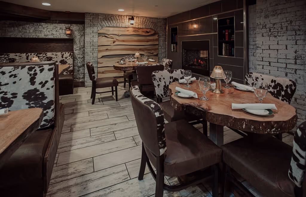 Elegant restaurant interior featuring wooden tables, cow-print chairs, and a cozy fireplace, creating a warm, inviting atmosphere.